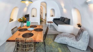 A modern interior with a wooden dining table, woven chairs, a grey sofa, and a unique arched ceiling design.