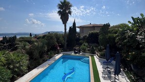 A swimming pool with a dolphin design, surrounded by greenery and a patio area with chairs and umbrellas.