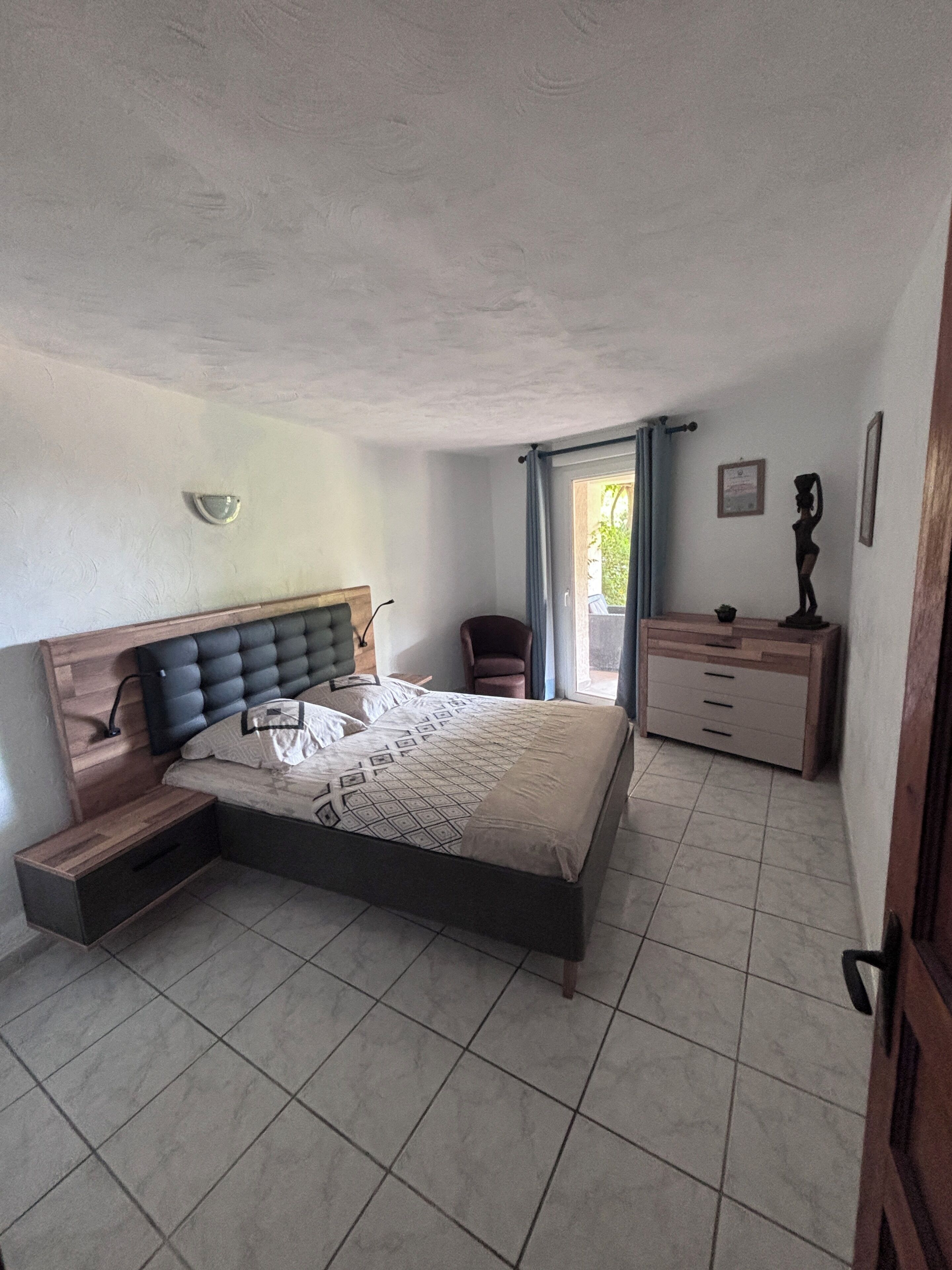 Ein Schlafzimmer mit einem Bett, einem Sessel, einem Schminktisch und einem Fenster mit Vorhängen.