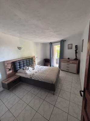 A bedroom with a bed, a chair, a dresser, and a window with curtains.