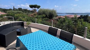An outdoor patio with a table covered in a blue textured tablecloth, surrounded by wicker furniture.