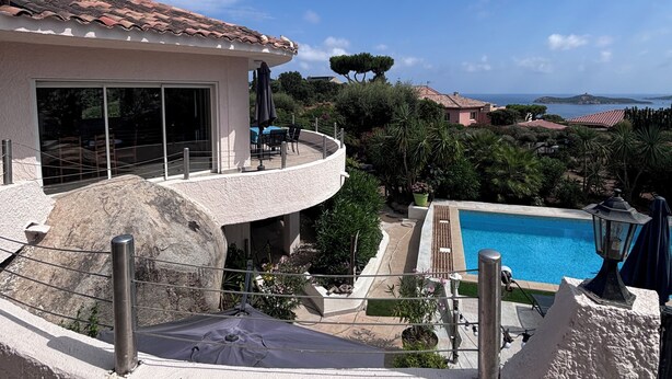 A poolside view with a clear sky, a building with a tiled roof, and a view of the sea.
