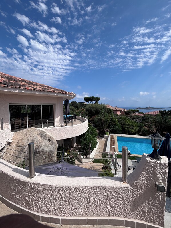 A poolside view with a clear sky, a building with a tiled roof, and a view of the sea.