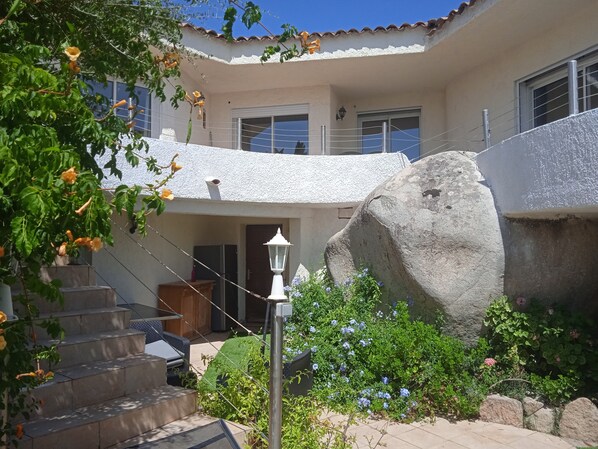 A two-story building with a white exterior, a large rock in the foreground, and a staircase leading to the upper level.