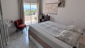 A bedroom with a bed, a chair, a fan, a map on the wall, and a view through a window.
