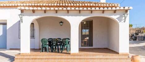 A building with a tiled roof, white walls, and a covered patio area with a table and chairs.