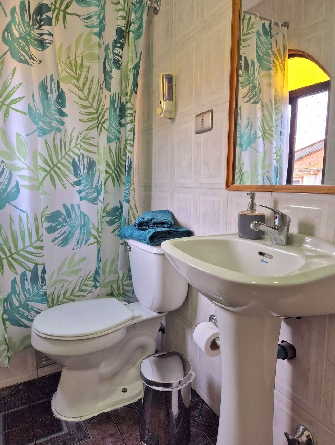 A bathroom with a toilet, sink, and shower curtain with a leaf pattern.