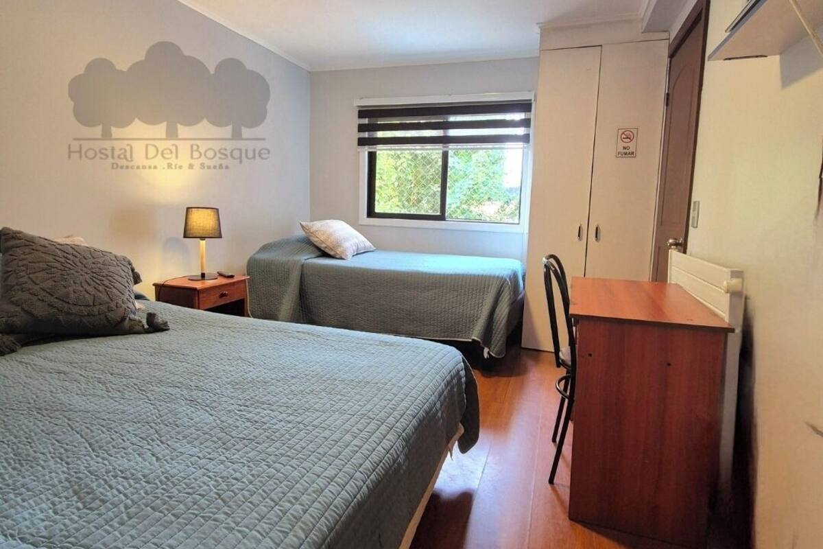 Ein Hotelzimmer mit zwei Betten, einem Nachttisch, einer Lampe, einem Fenster mit Jalousien, einem Kleiderschrank und einem Rauchverbotsschild.