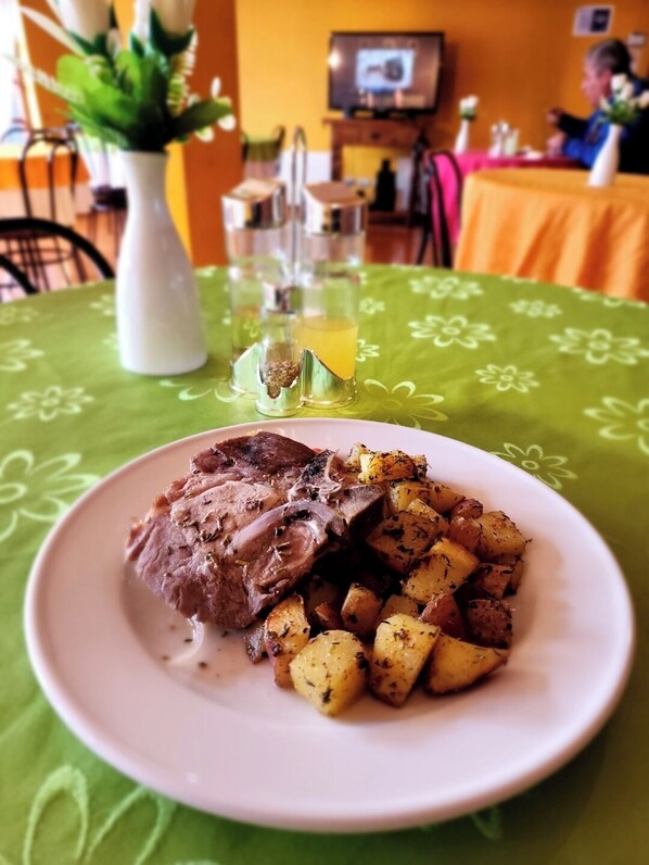 Un plato de carne asada y papas sobre una mesa con mantel verde.