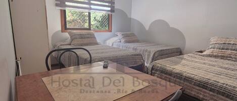 A small hotel room with two beds, a wooden table, and a window with blinds.