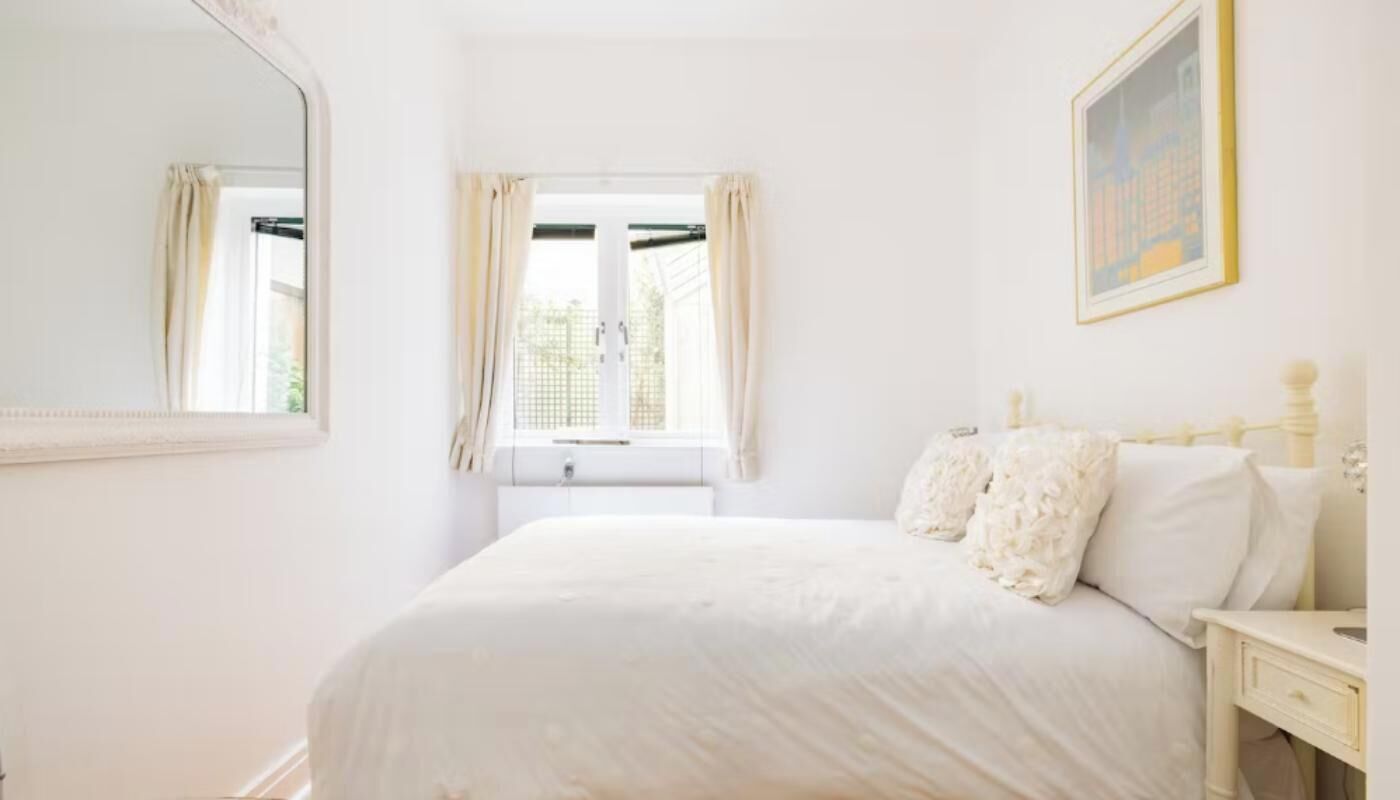 A bedroom with a bed, a window with curtains, a bedside table, and a wall-mounted picture.