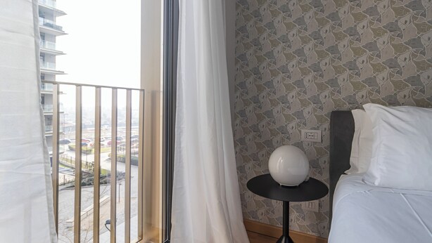 Une chambre d’hôtel avec un balcon, un lit avec une literie blanche, une table ronde blanche et un papier peint à motifs.