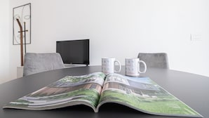 Une table de conférence avec un magazine ouvert, deux tasses blanches portant le logo « Italianway », un téléviseur noir et des chaises grises.