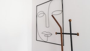 Une œuvre d’art abstraite encadrée, au design minimaliste, représentant un simple contour de visage et un bâton de bois appuyé contre celui-ci.