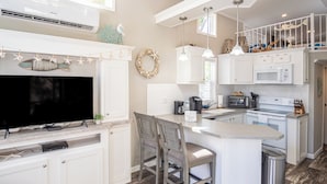 Una cocina moderna con armarios blancos, una isla central con taburetes y un microondas integrado, además de un televisor de pantalla plana grande.