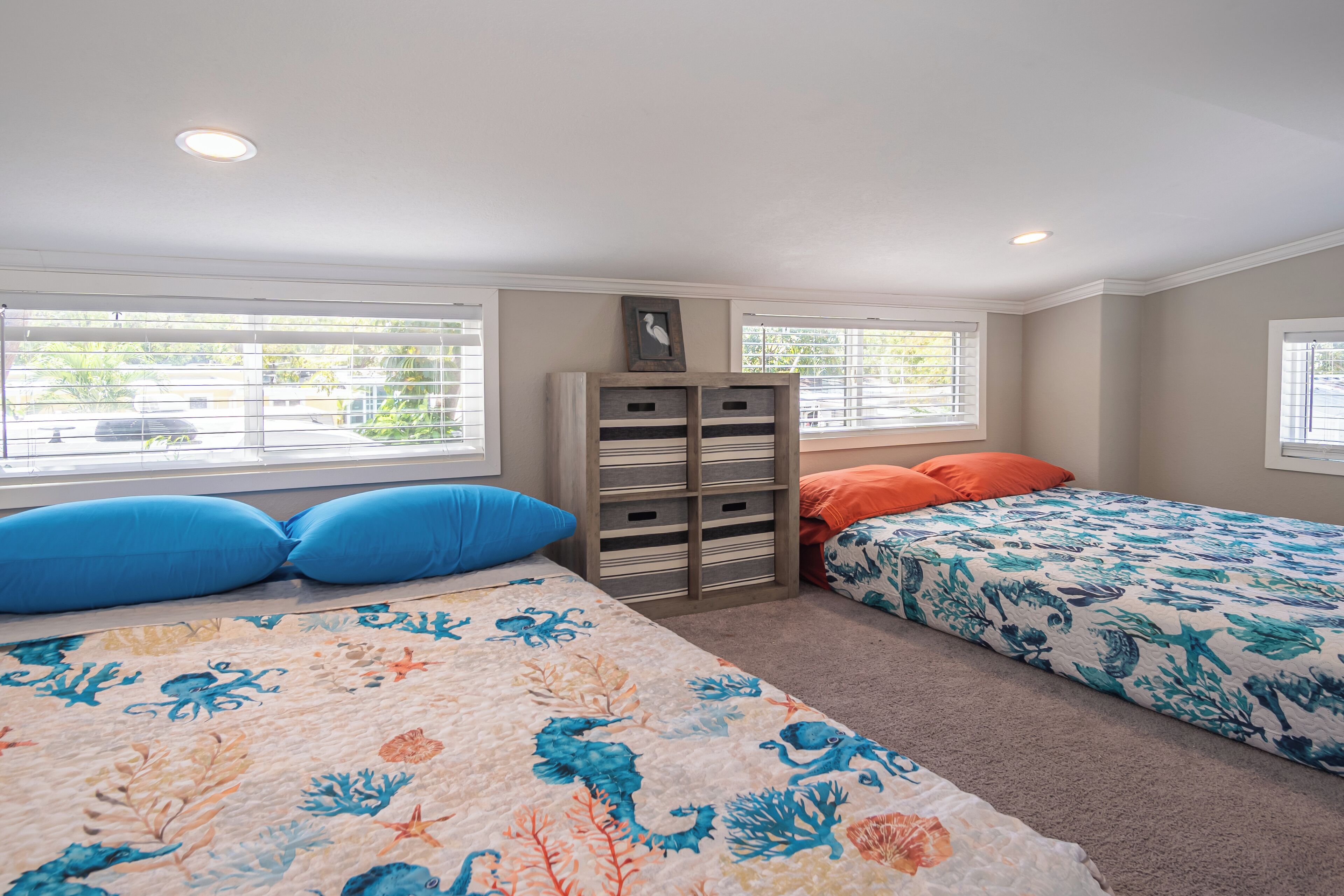 Une chambre avec deux lits, un meuble de rangement en bois et des fenêtres équipées de stores.