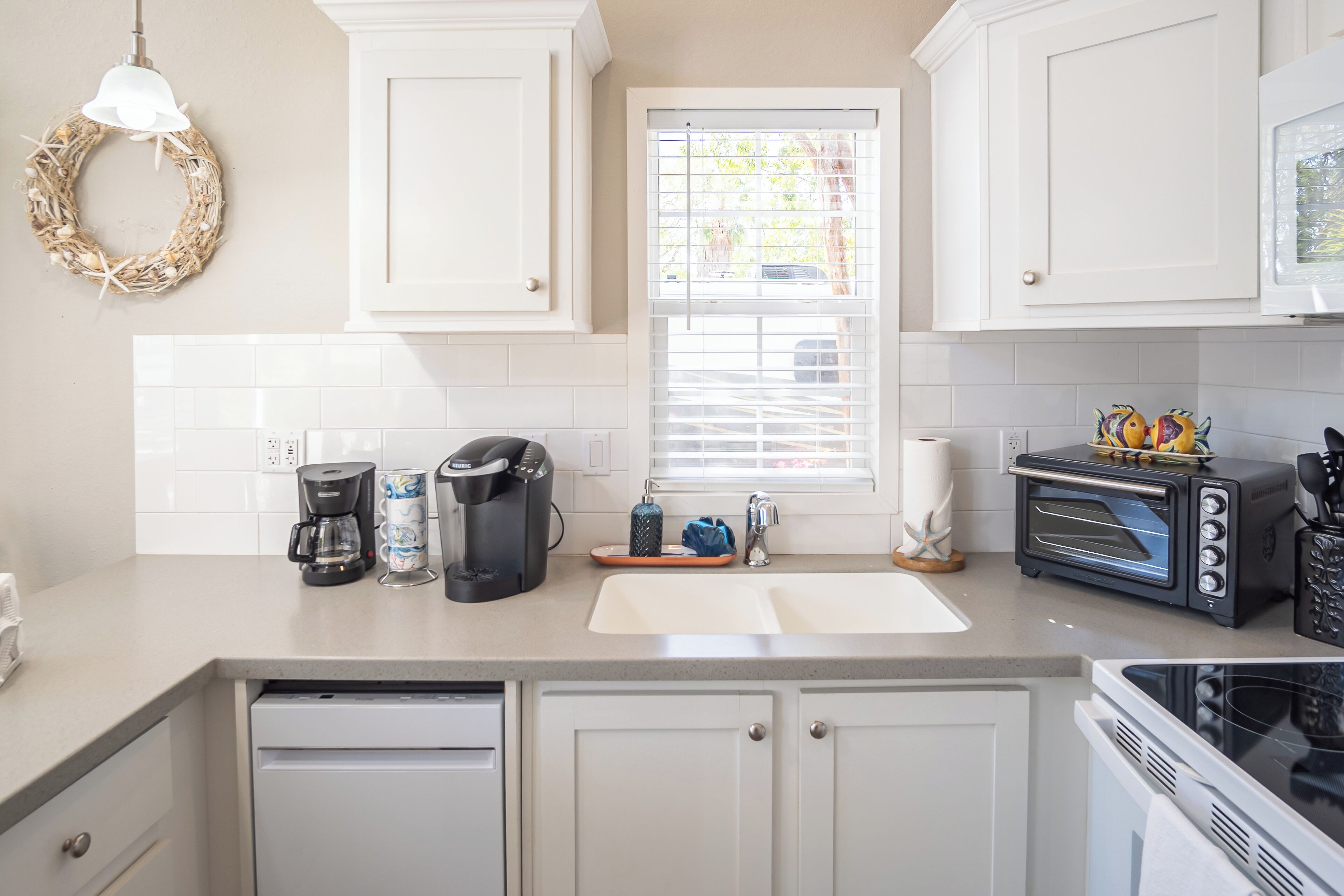 A kitchen with white cabinets, a built-in oven, a microwave, a coffee maker, and a window with blinds.