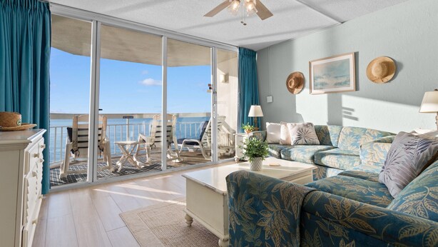 A spacious living room with a large sliding glass door leading to a balcony, a ceiling fan, and a sofa with patterned upholstery.