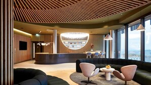 A modern lobby with a curved reception desk, seating area with sofas and chairs, and large windows offering a view. - Wald.Weit Rheingau Hotel und Retreat (Kiedrich)
