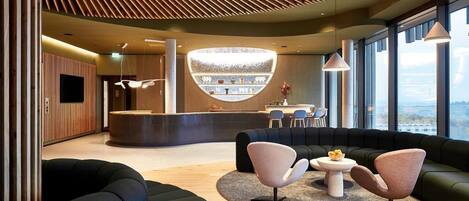 A modern lobby with a curved reception desk, seating area with sofas and chairs, and large windows offering a view.