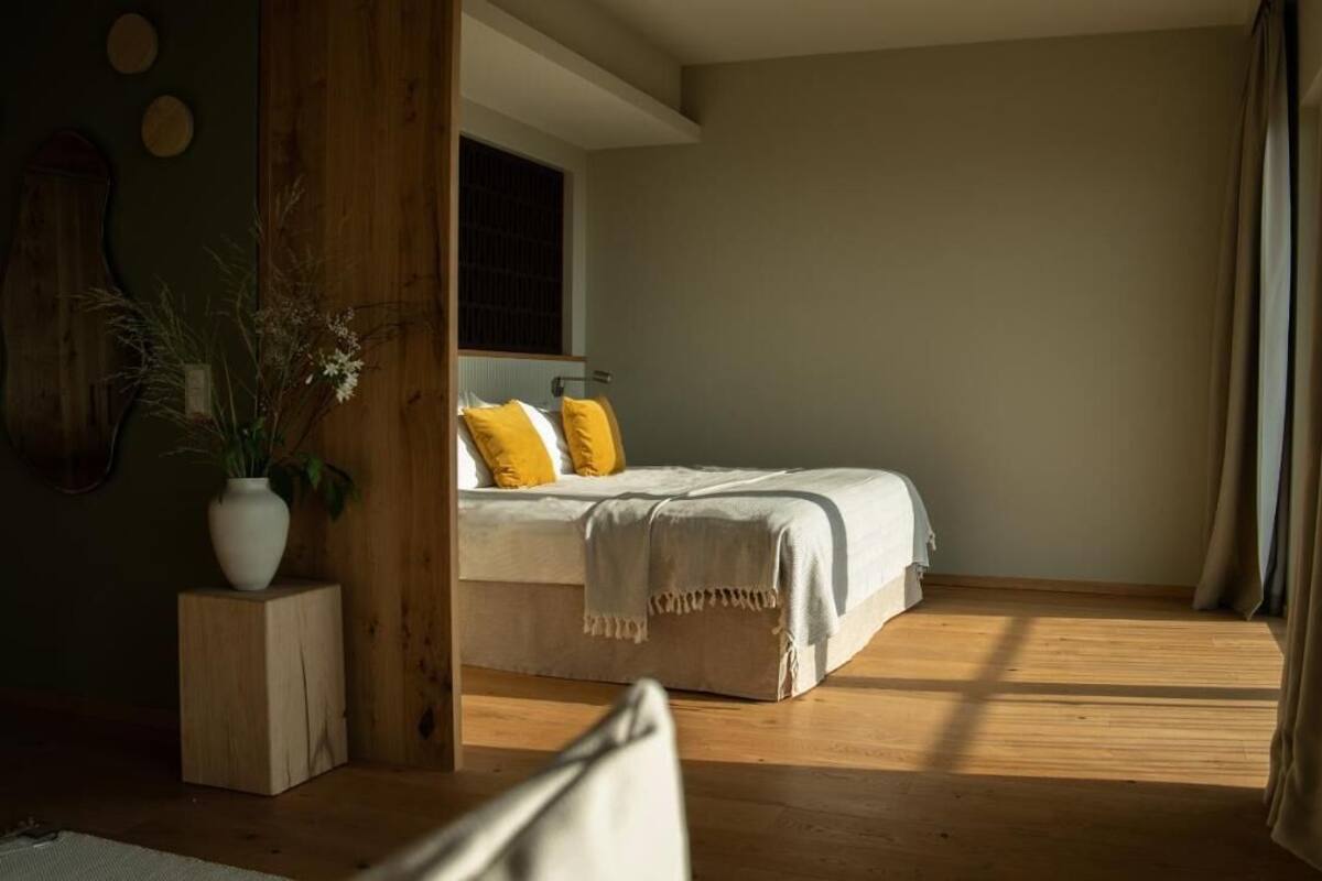 Ein Schlafzimmer mit Bett, Holzboden, Fenster und einer Pflanze.