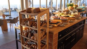 Mostrador de panadería con panes y pasteles varios, una estación de café y vistas de la ciudad.
