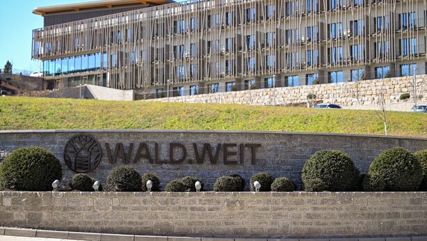 Un edificio moderno con un letrero que dice "WALD. WEIT" y un área ajardinada con arbustos bien cuidados.