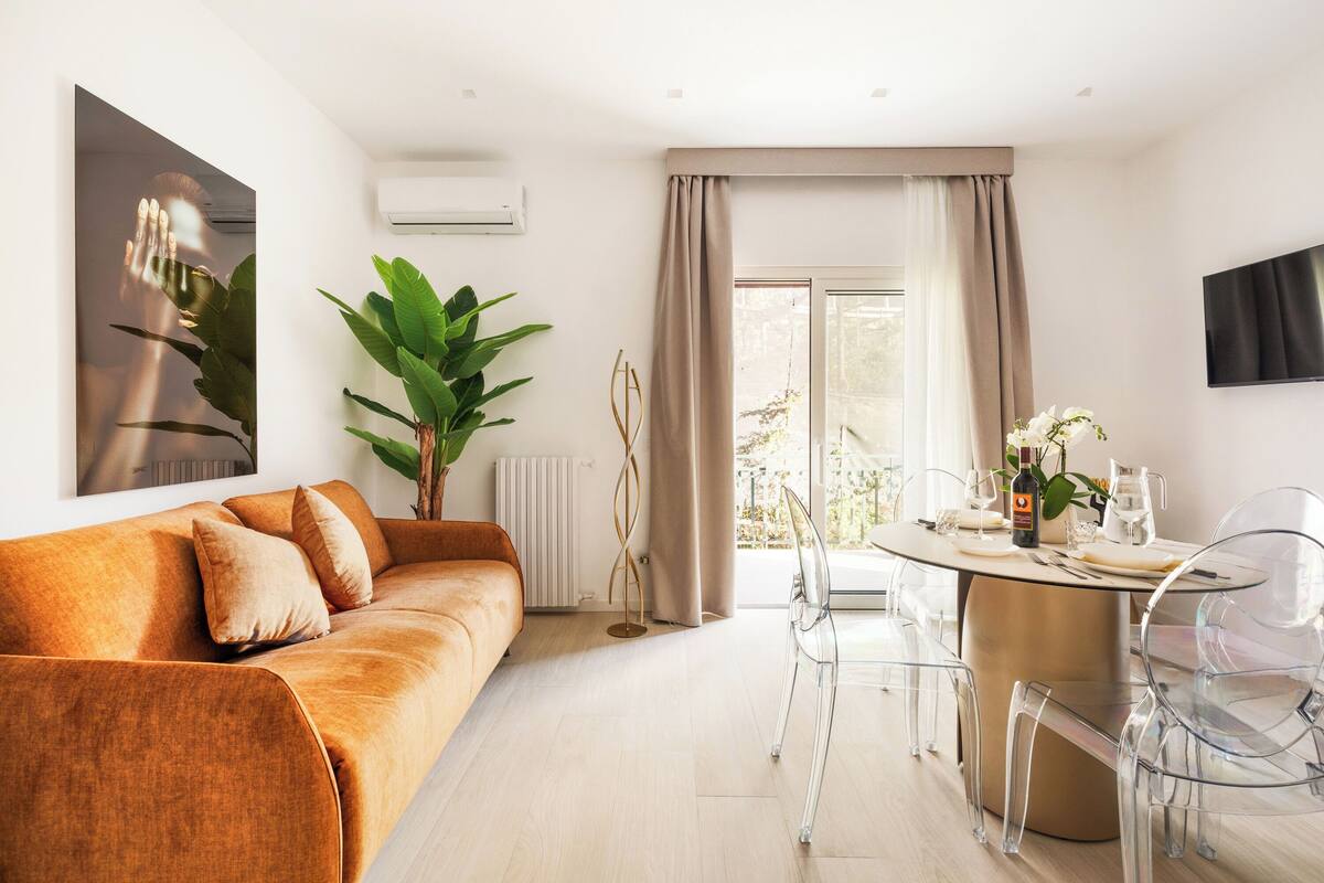 A modern living room with a sofa, clear chairs, a dining table, and a large window with curtains.