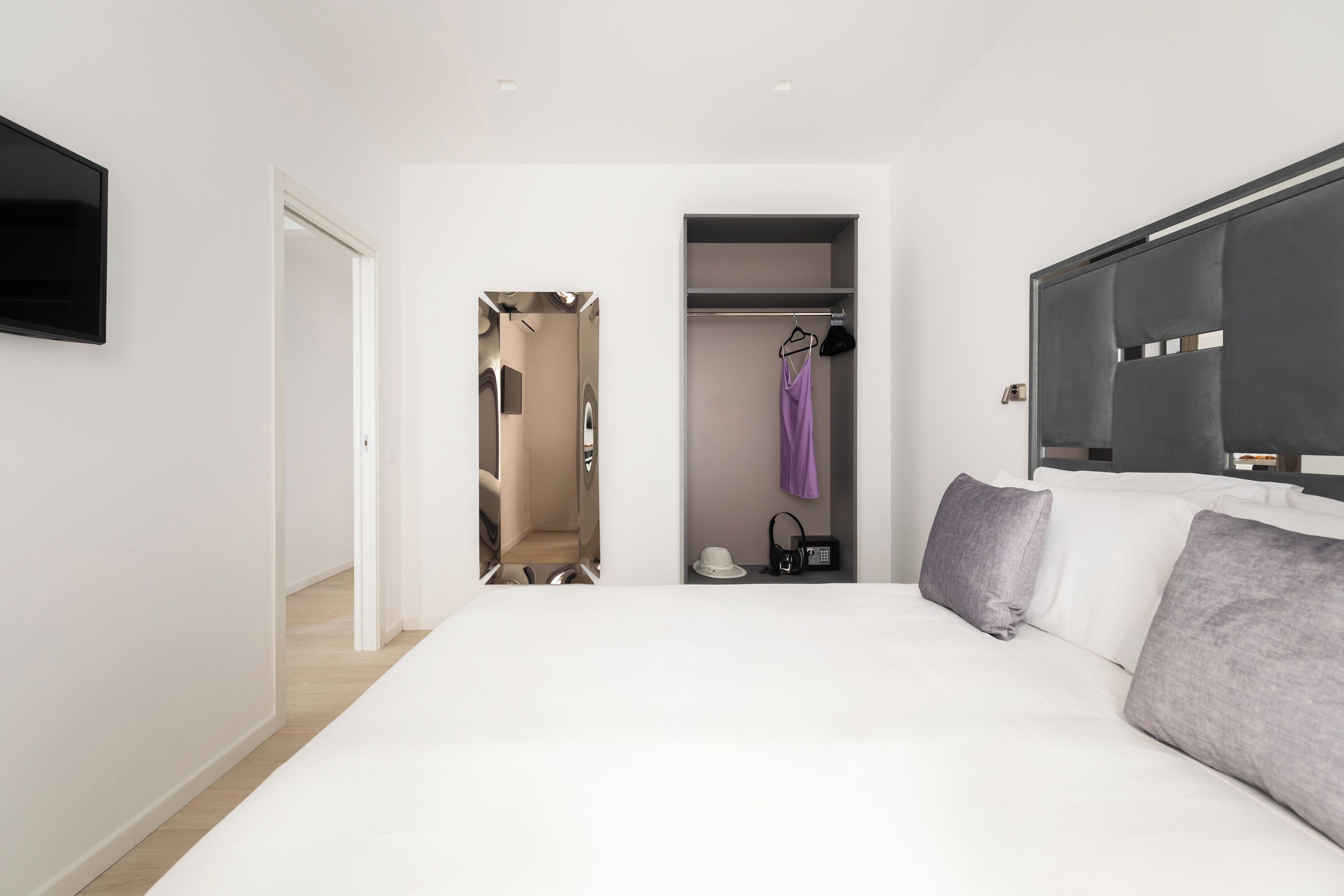 Un dormitorio moderno con una cama grande, un vestidor y un televisor montado en la pared.