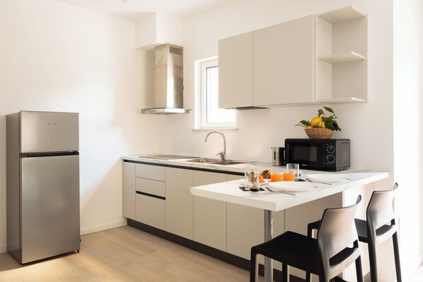 A modern kitchen with a stainless steel refrigerator, a microwave, a sink, and a dining area with two chairs. - YourHome - Aranci Prestige (Sorrento)
