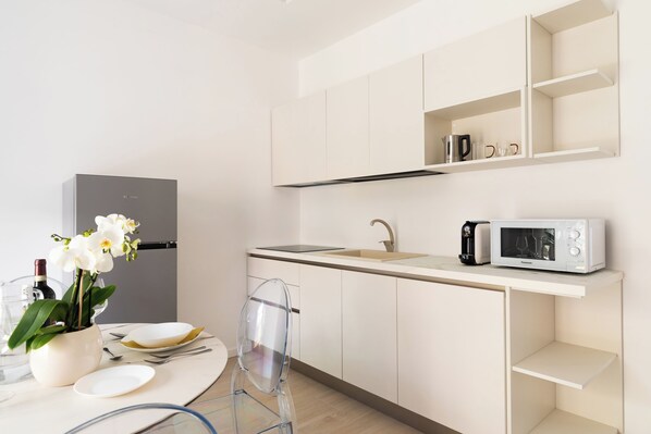 Una cocina moderna con armarios blancos, microondas y un lavamanos. Hay una mesa de comedor con un florero y una silla.