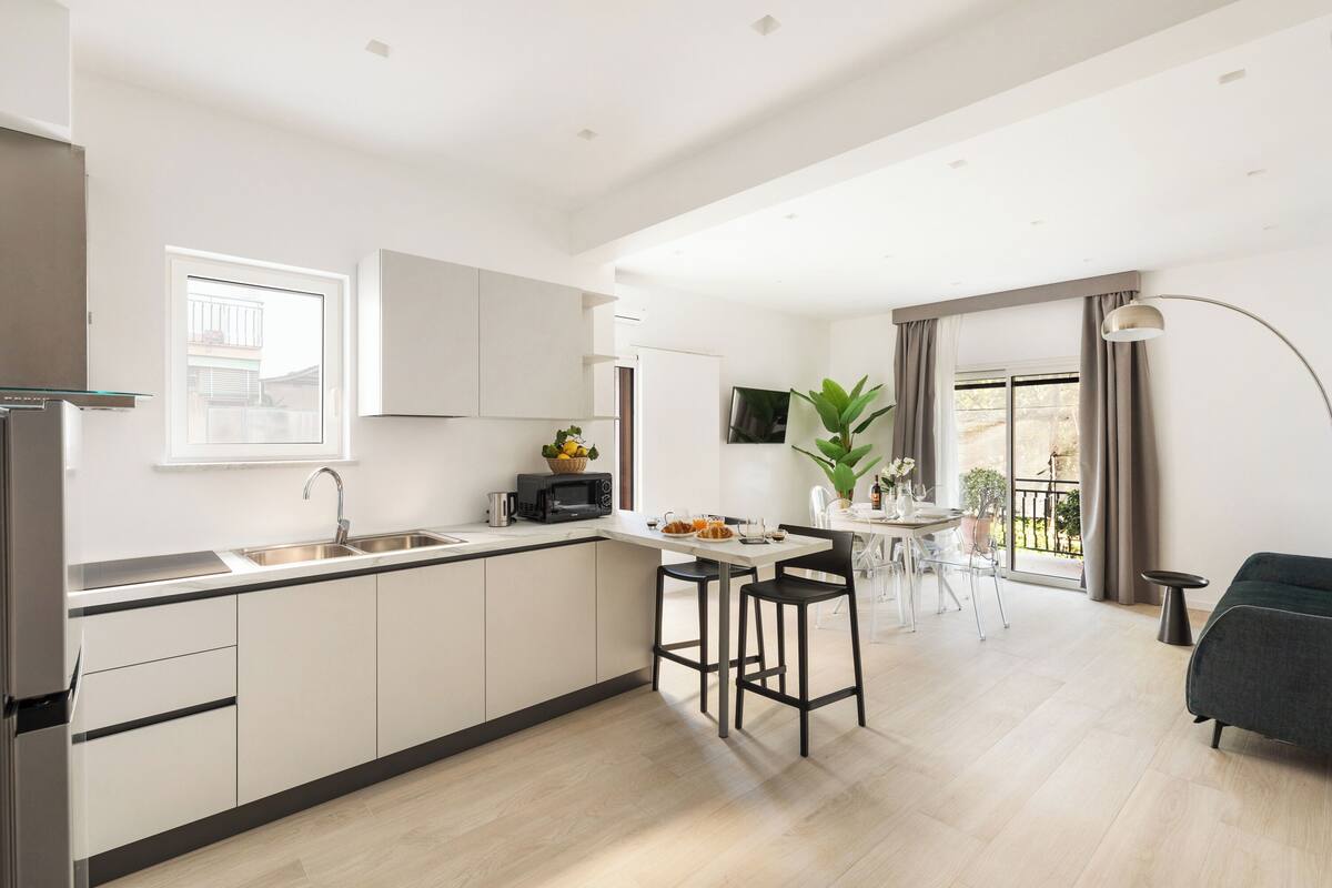 A modern kitchen with a central island, a dining area with a table and chairs, and a living area with a sofa and a lamp.