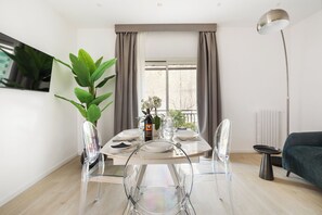 Un comedor moderno con una mesa redonda, sillas transparentes, una planta en maceta y vistas al exterior a través de una ventana con cortinas.