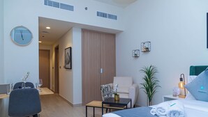 A modern hotel room with a bed, a desk, a chair, a small table, a plant, and a wall clock. - Bloomfields Fantastic STU Azizi Riviera (Dubai)