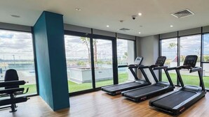 A gym with treadmills, a bench press, and large windows offering a view of the outdoors. - Bloomfields Fantastic STU Azizi Riviera (Dubai)