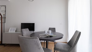 Ett modernt vardagsrum med ett runt bord, två grå fåtöljer, en platt-TV och en tidning.
