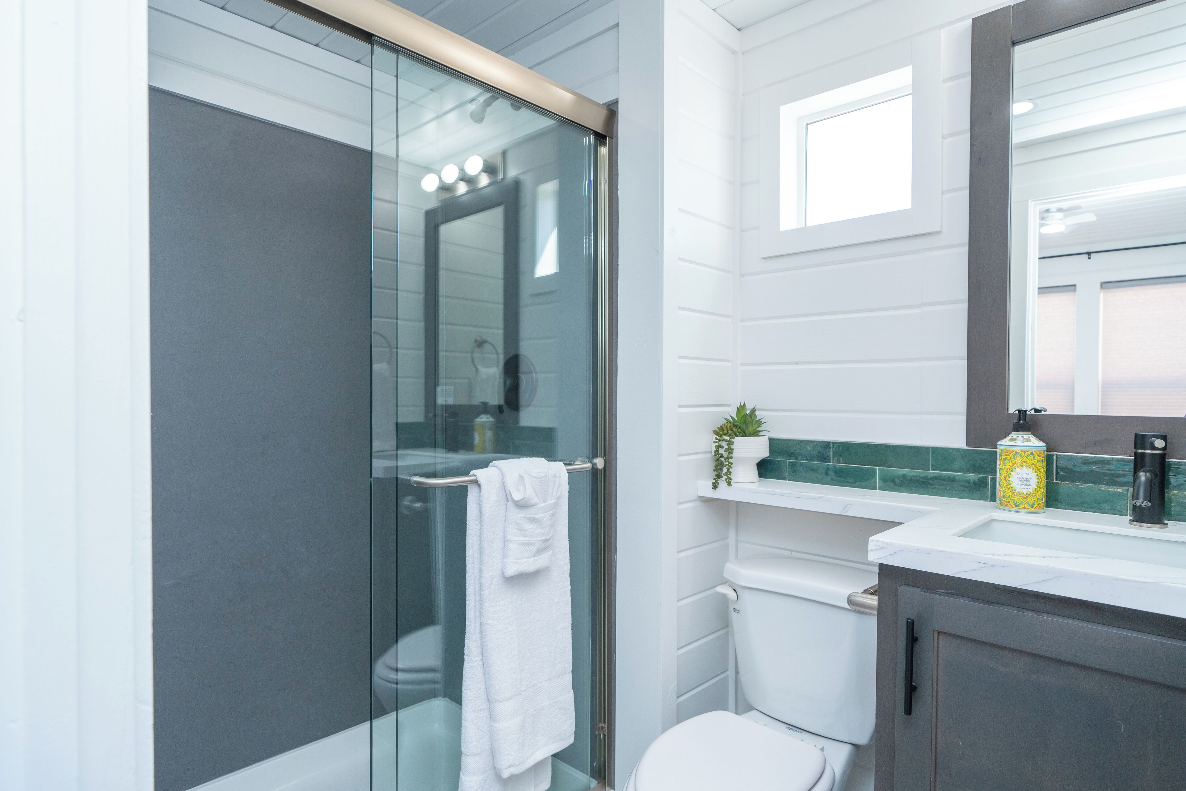 Une salle de bain moderne avec une douche à parois de verre, des toilettes blanches et un meuble-lavabo avec un miroir.