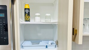 Eine Küche mit Mikrowelle, Herd, Spüle und einem Regal mit einer Dose Bio-Canolaöl, zwei Glasbehältern und einem blauen Geschirrgestell.