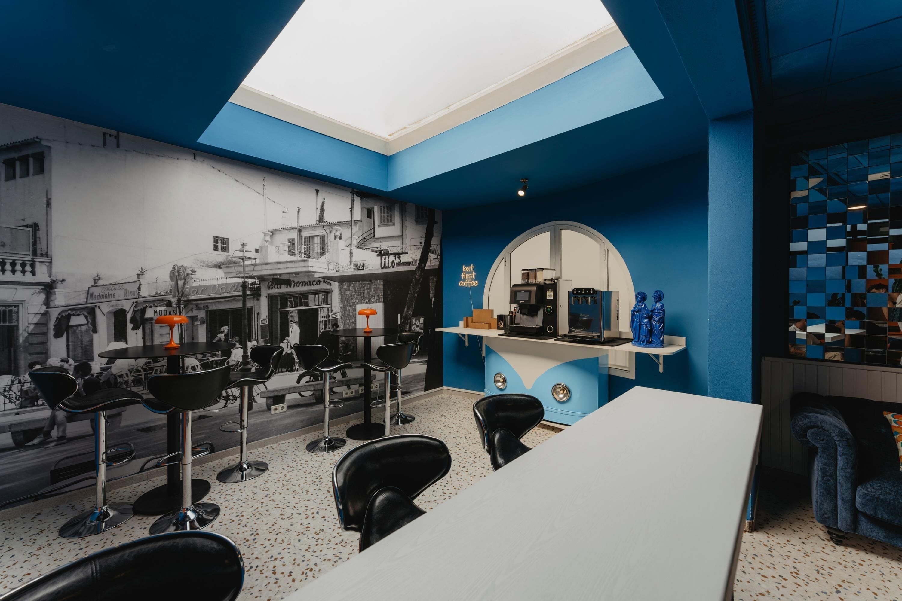 Ein Café mit Wandmalerei einer Straßenszene, einem weißen Tisch, schwarzen Barhocker und einer blauen Akzentwand.