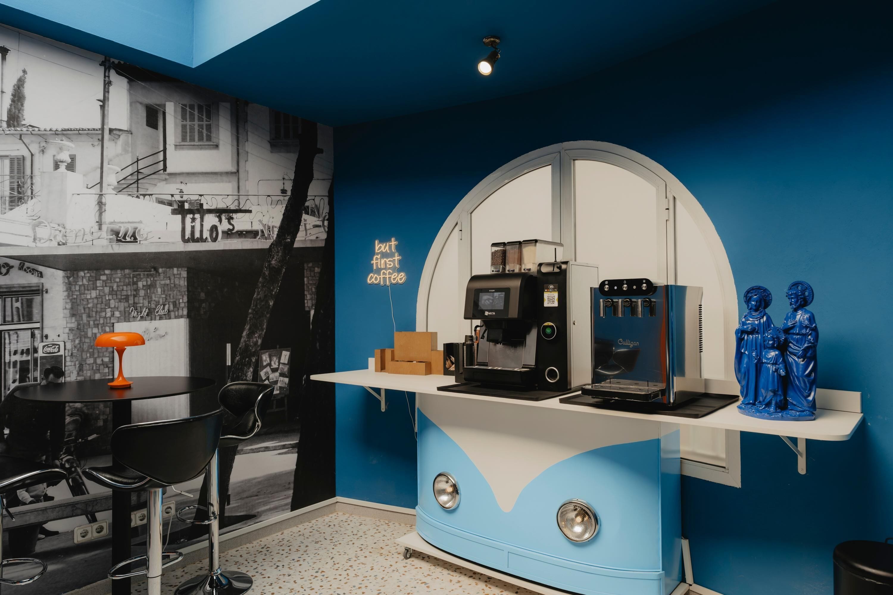 A modern bar area with a blue and white color scheme, featuring a coffee machine, a mirror, and a statue.