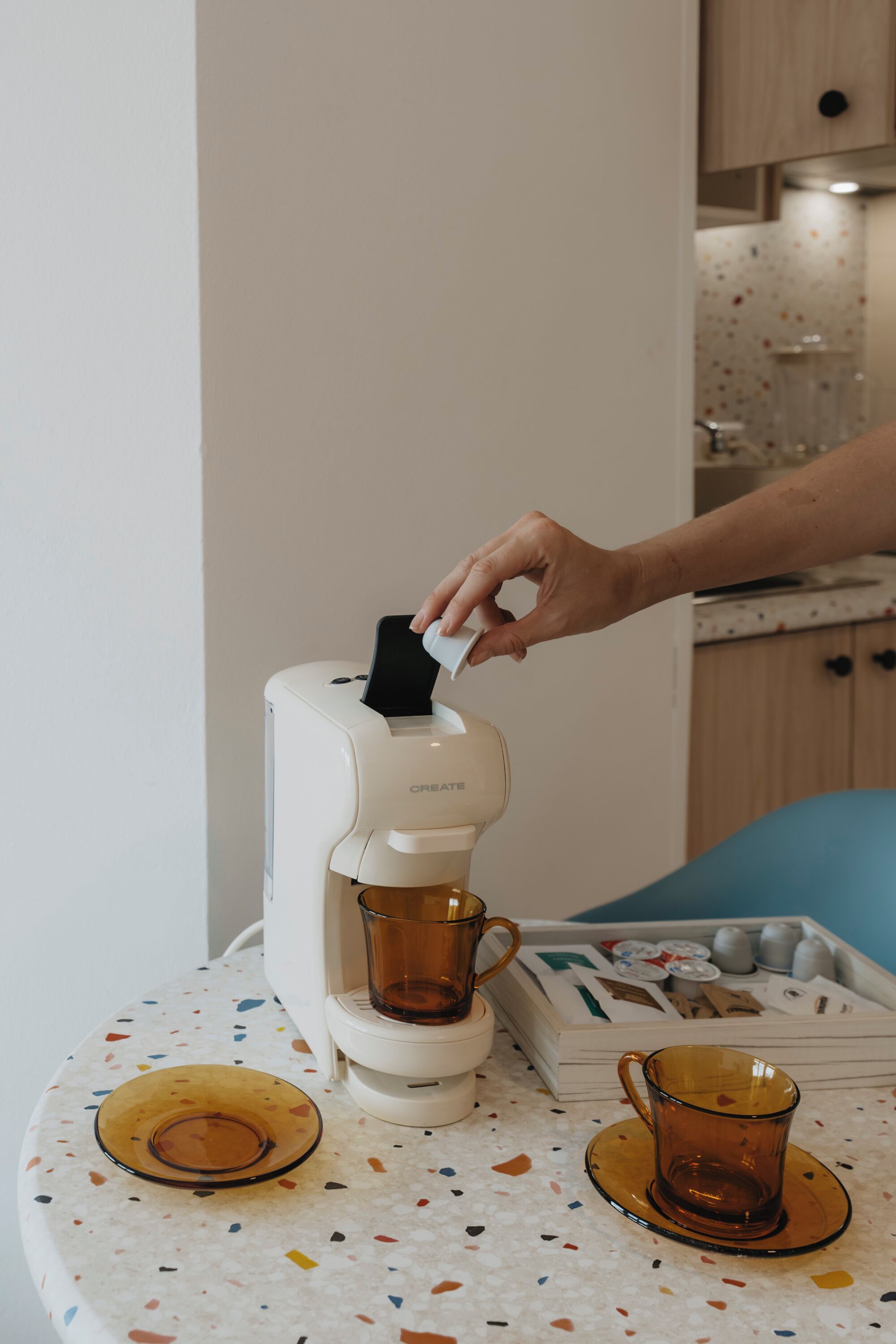 Una cafetera sobre una mesa con dos tazas y una bandeja de cápsulas de café.