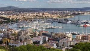 Un puerto deportivo lleno de barcos, rodeado por un paisaje urbano con edificios y una colina distante.