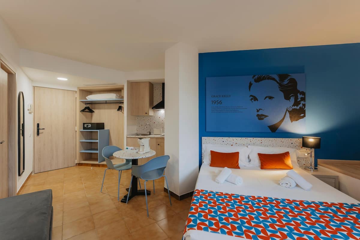 Una habitación de hotel con cama, escritorio, silla y kitchenette.