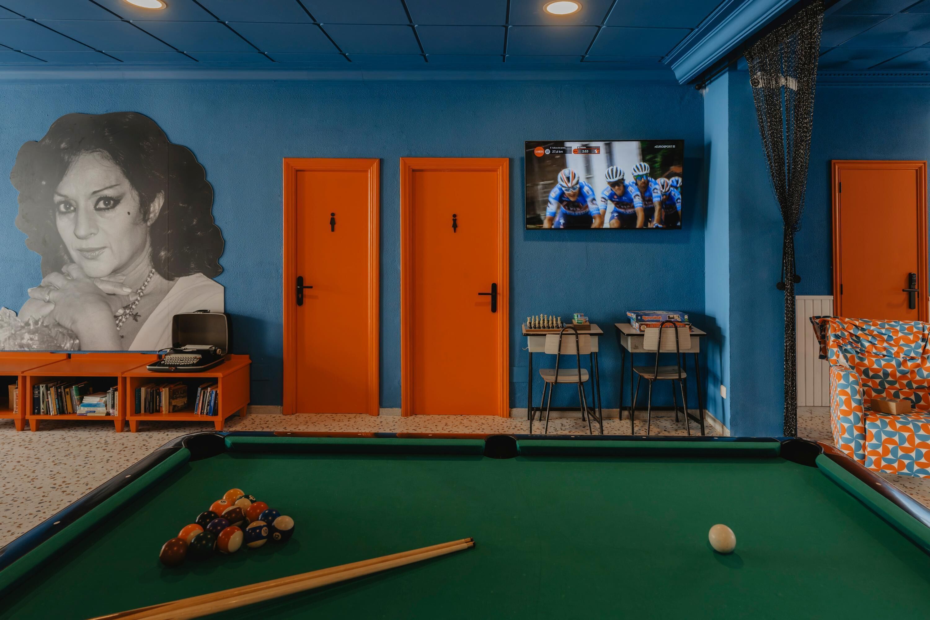 A pool table with balls, a billiard cue, and a television displaying a cycling event.