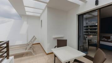 A balcony with a white table and wicker chairs, a glass door leading to a bedroom, and a skylight.