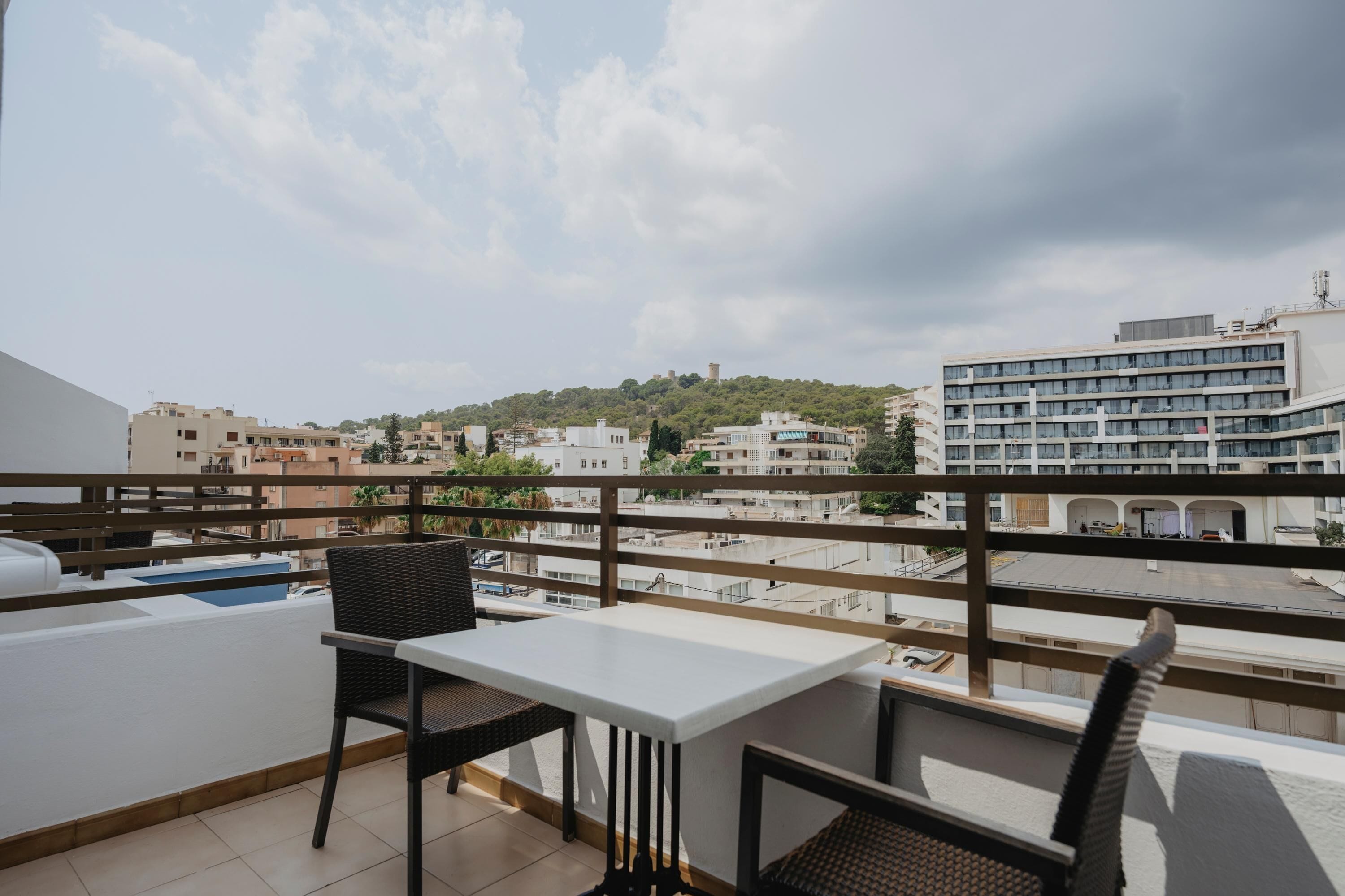 Een balkon met een tafel en stoelen, met uitzicht op een stadsbeeld met gebouwen en een heuvel.