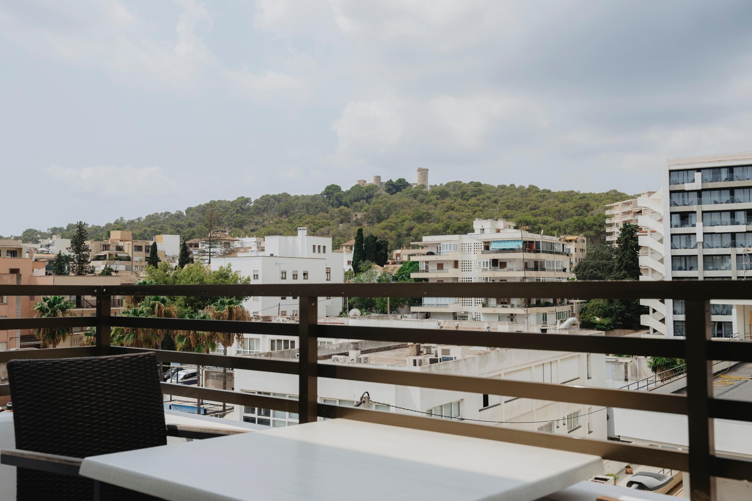 A balcony with a view of a cityscape, including buildings and a hill with a tower.