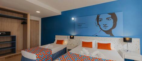A hotel room with two beds, a blue accent wall, and a portrait of Maria Callas.
