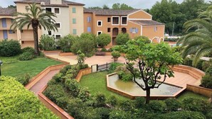 A residential building with multiple balconies, a central courtyard with a water feature, and surrounding greenery. - On the water: XXL Terrace, Paddle, Bikes & A/C. New 2025 + 2 Secure Garages (Cogolin)