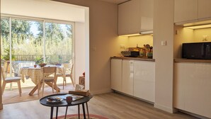 A compact kitchen with a microwave, sink, and cabinets. There is a dining area with a table and chairs, and a view of greenery through a sliding door. - On the water: XXL Terrace, Paddle, Bikes & A/C. New 2025 + 2 Secure Garages (Cogolin)